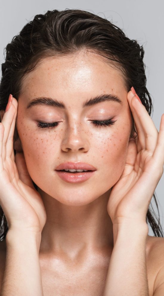 Woman with clear, freckled skin touching her temples with eyes closed